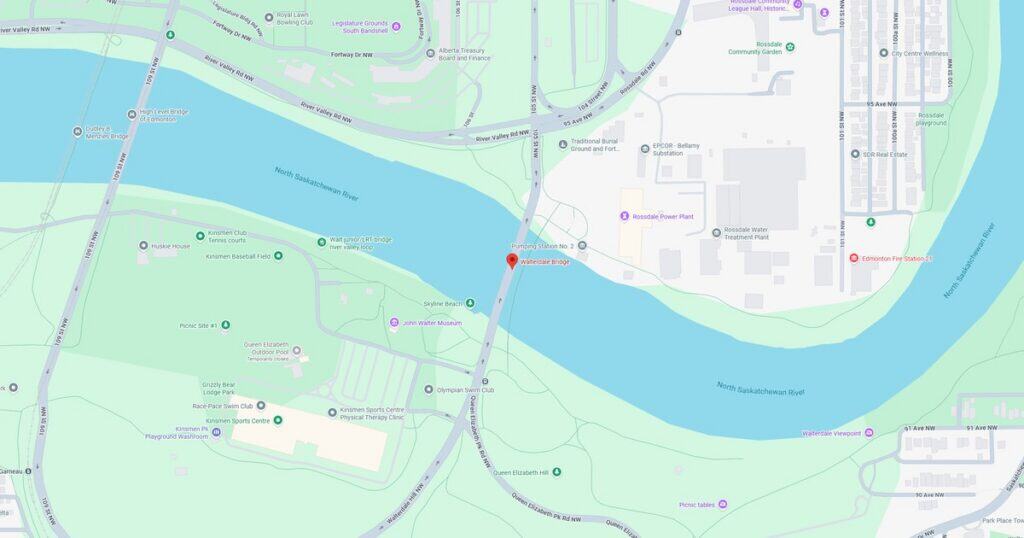 Scenic riverfront park with walking trails and a bridge crossing the river, surrounded by lush greenery and urban infrastructure.